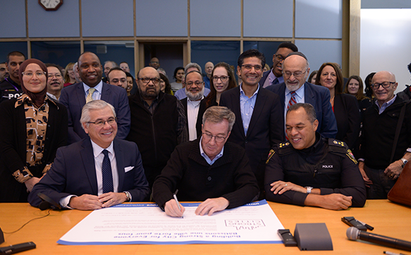 Mayor, police chief, and president of United Way sign a declaration at City Hall, surrounded by members of the United for All coalition