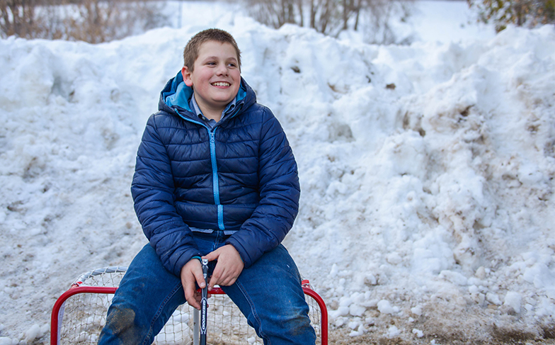 Boy sitting on top of mini hockey net, outside.