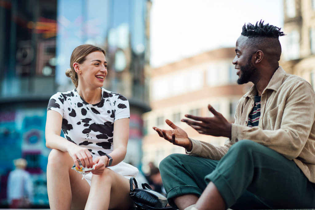 A photo of two people sitting outside on some steps chatting together.