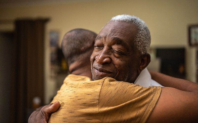 A photo of two older friends hugging each other.