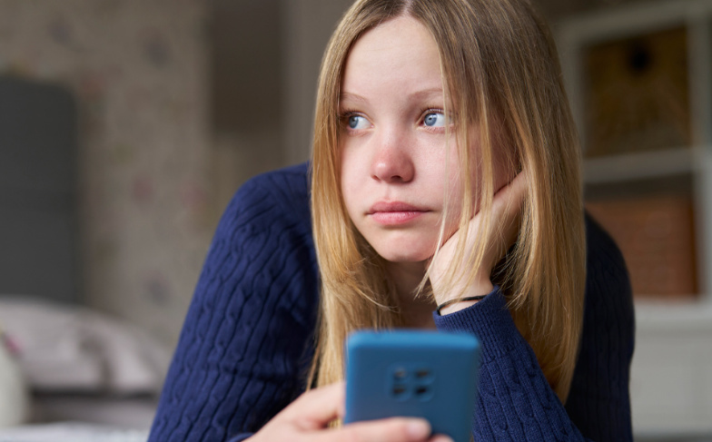 A photo of a girl sitting on her bed surfing on her mobile device.