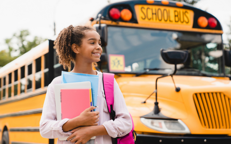 A photo of a girl getting off the school bus holder her books.